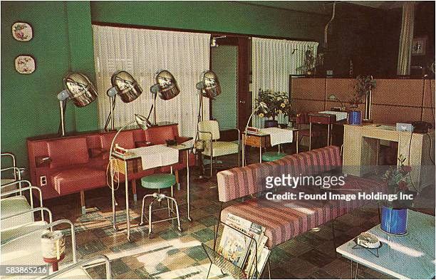 Vintage color photograph of the empty interior of a Beauty Parlor featuring hair drying stations with large silver dryers, a manicurist’s table, and...