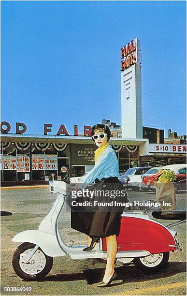 Vintage color photograph of a chic woman in a skirt, scarf and white sunglasses balancing on a red and white motor scooter with a bag of groceries on...