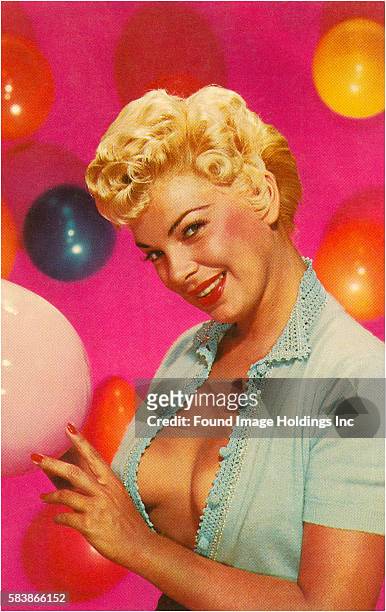 Vintage color studio photograph of a coyly smiling buxom blonde with an unbuttoned demure blue blouse revealing braless breasts, all against a hot...
