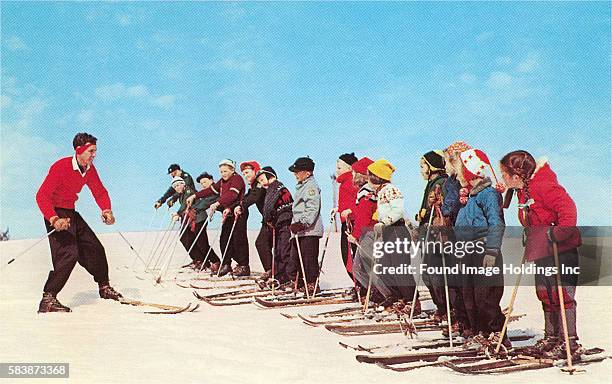 Vintage photograph of a male ski instructor giving a ski lesson to a group of children in the 1960s.