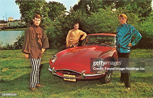 Vintage photograph of three young men in Mod attire standing around a red sports car outside in the 1960s.