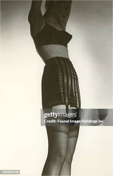 Vintage photograph of a woman with her arms up; wearing a bra, girdle, garters, and stockings for an advertisement, 1940s.