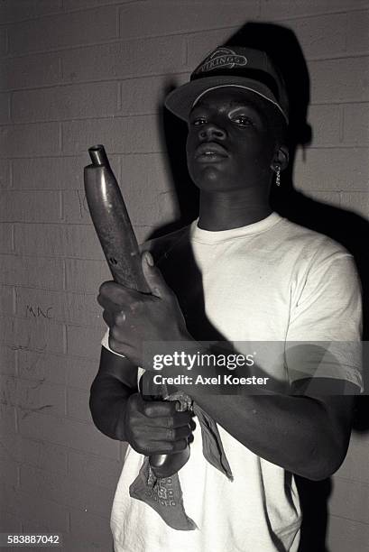 Member of the Grape Street Crips poses with his shotgun and wears his gang's signature Vikings baseball cap and purple bandana. The Grape Street...