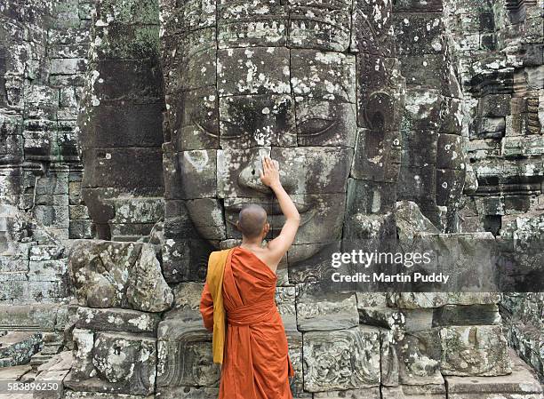 buddhist monk in front of stone carved face - philosophy stock pictures, royalty-free photos & images
