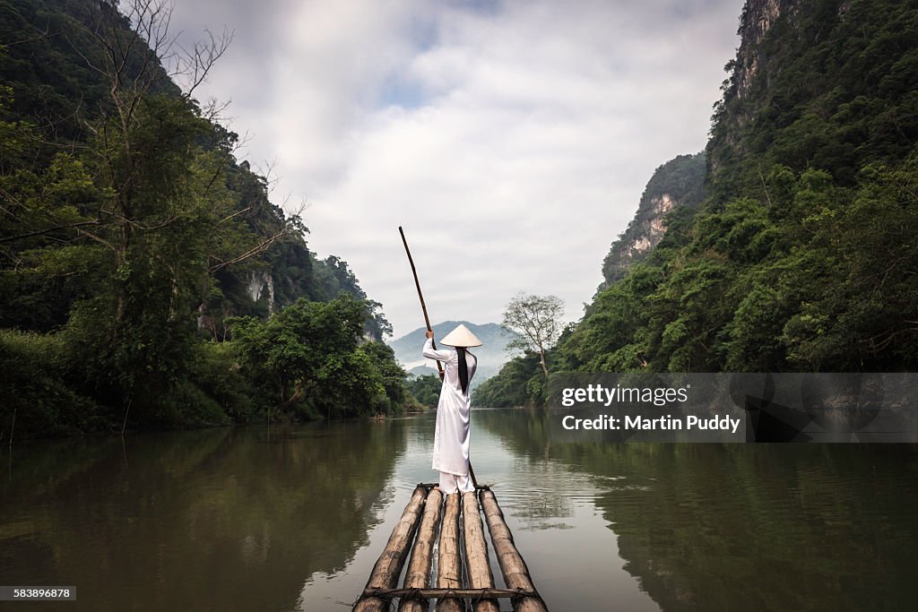 Young woman punting bamboo raft along river