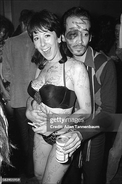 An unidentified man with a can of beer stands behind embraces American sex educator and performance artist Annie Sprinkle, who is dressed in...