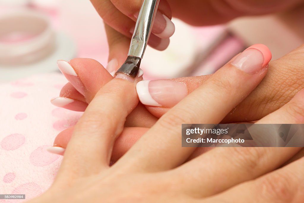 Manicure applying nail gloss on female fingernails