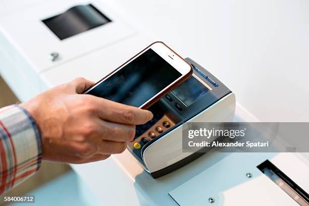 man making purchases through mobile payment with his smartphone and terminal - pago por móvil fotografías e imágenes de stock