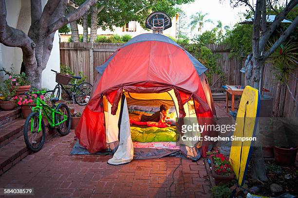 boy reading in tent in side yard of house - boys camping stock-fotos und bilder