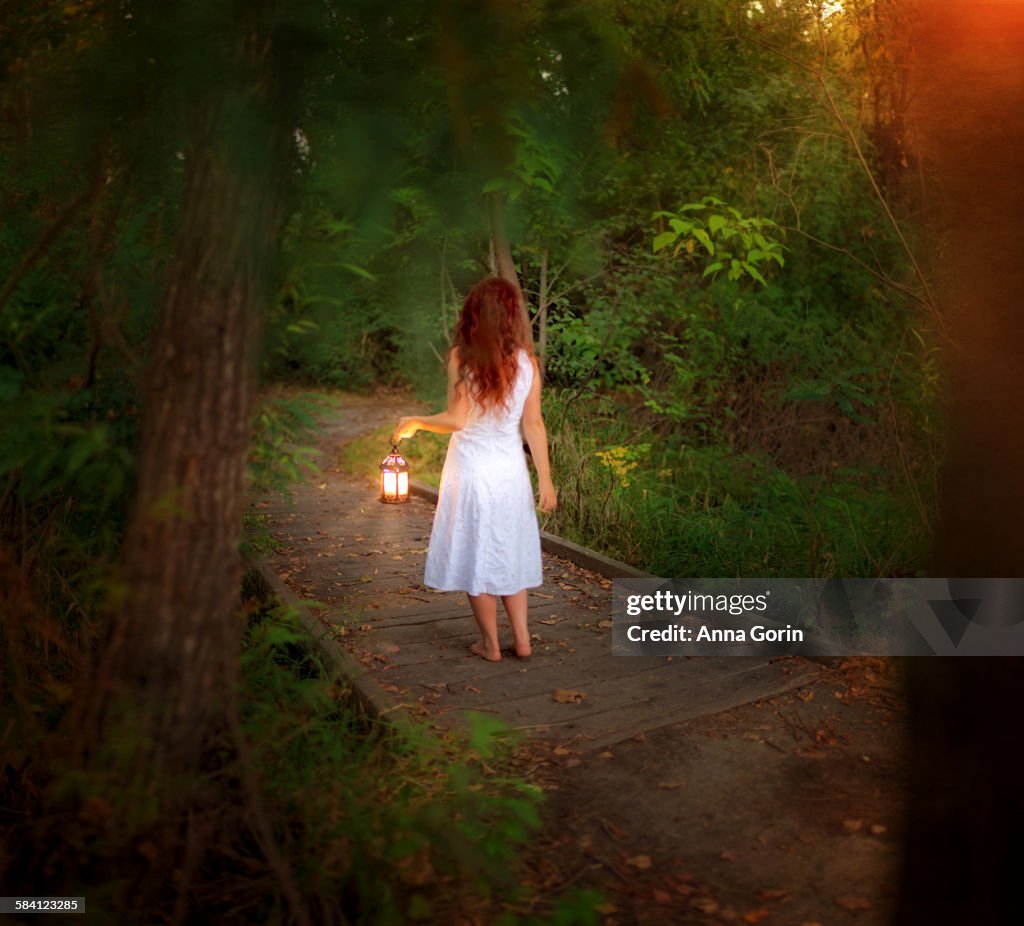 Barefoot girl in forest with lantern, rear view