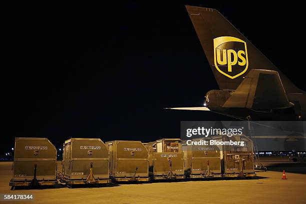 Package containers sit in a row next to a Boeing Co. 747 cargo plane during the night package sort at the United Parcel Service Inc. Worldport...