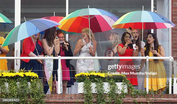 Racegoers shelter under multicoloured umbrellas as they watch the racing on Ladies Day of the Qatar Goodwood Festival at Goodwood Racecourse on July...