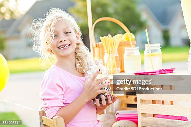 cute smiling girl holding up her earnings from selling lemonade - kids making money stock pictures, royalty-free photos & images