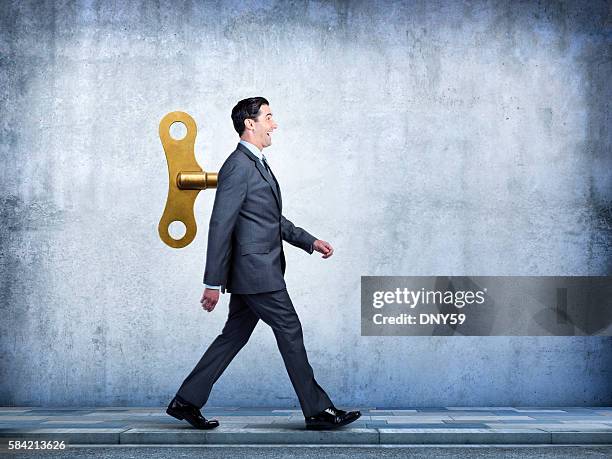 happy businessman walking with wind up key in his back - wind up toy stock pictures, royalty-free photos & images