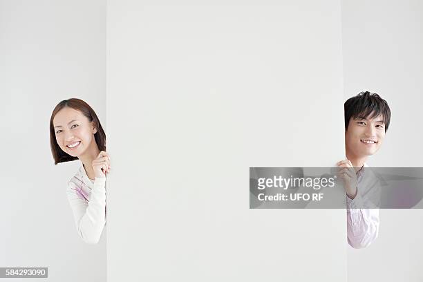 young couple peeking from wall - spähen stock-fotos und bilder
