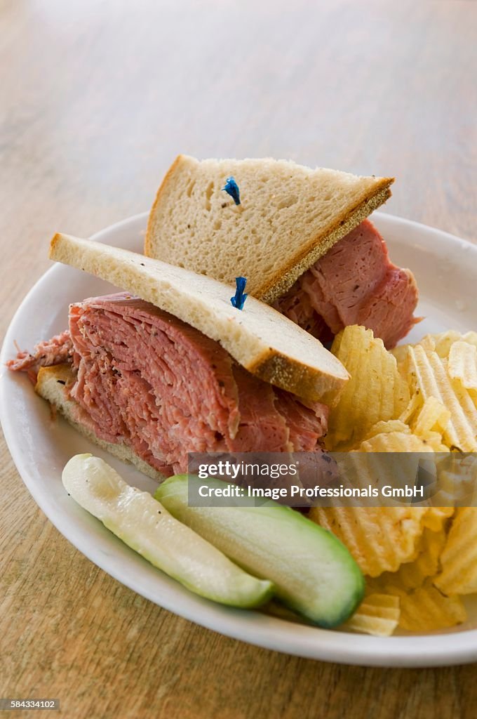 A corned beef sandwich with crisps and pickled gherkins