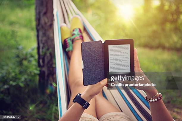 beautiful girl is reading e-book in the hammock - e reader stock pictures, royalty-free photos & images