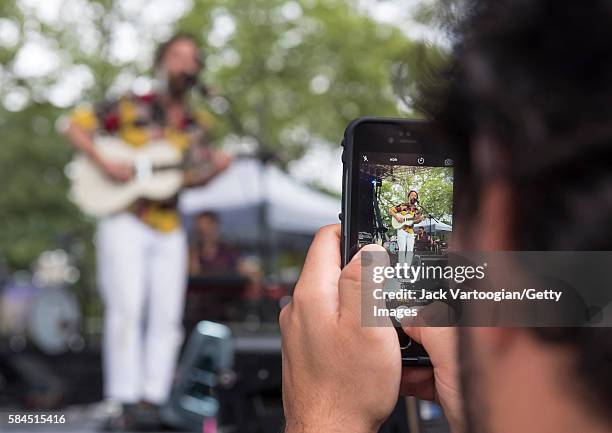 View over the shoulder of an unidentified audience member who uses his smartphone to photograph Brazilian musician Rodrigo Amarant on stage at the...