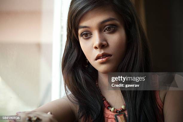 serene girl looking away with blank expression sitting near window. - next to stock pictures, royalty-free photos & images