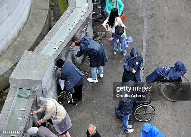 Pilgrims filling bottles with healing water at spring of the Sanctuary of Our Lady of Lourdes, Pyrenees, France.