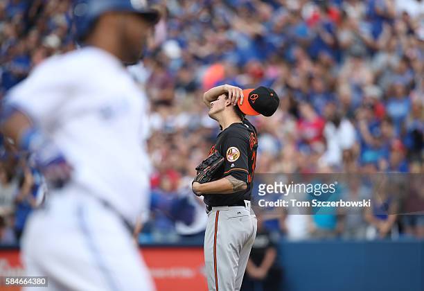 Kevin Gausman of the Baltimore Orioles reacts after giving up a solo home run to Edwin Encarnacion of the Toronto Blue Jays who circles the bases in...
