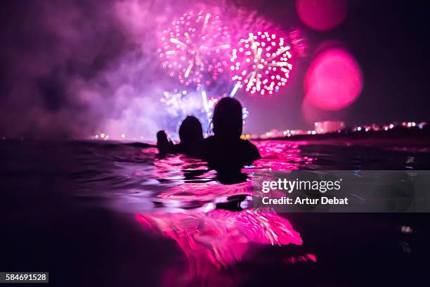 girls having fun enjoying and contemplating the colorful fireworks at night taking a bath in the beach with colorful reflection. - hot spanish women ストックフォトと画像
