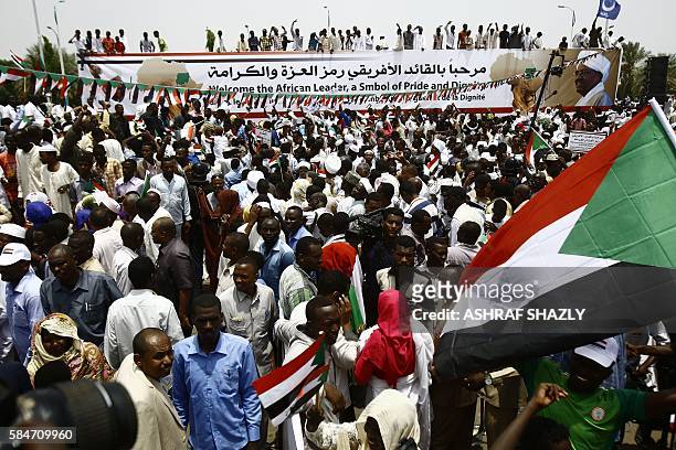 Supporters of Sudanese President hold national flags and deploy a banner during a ceremony in his honour upon his return in the country from Ethiopia...