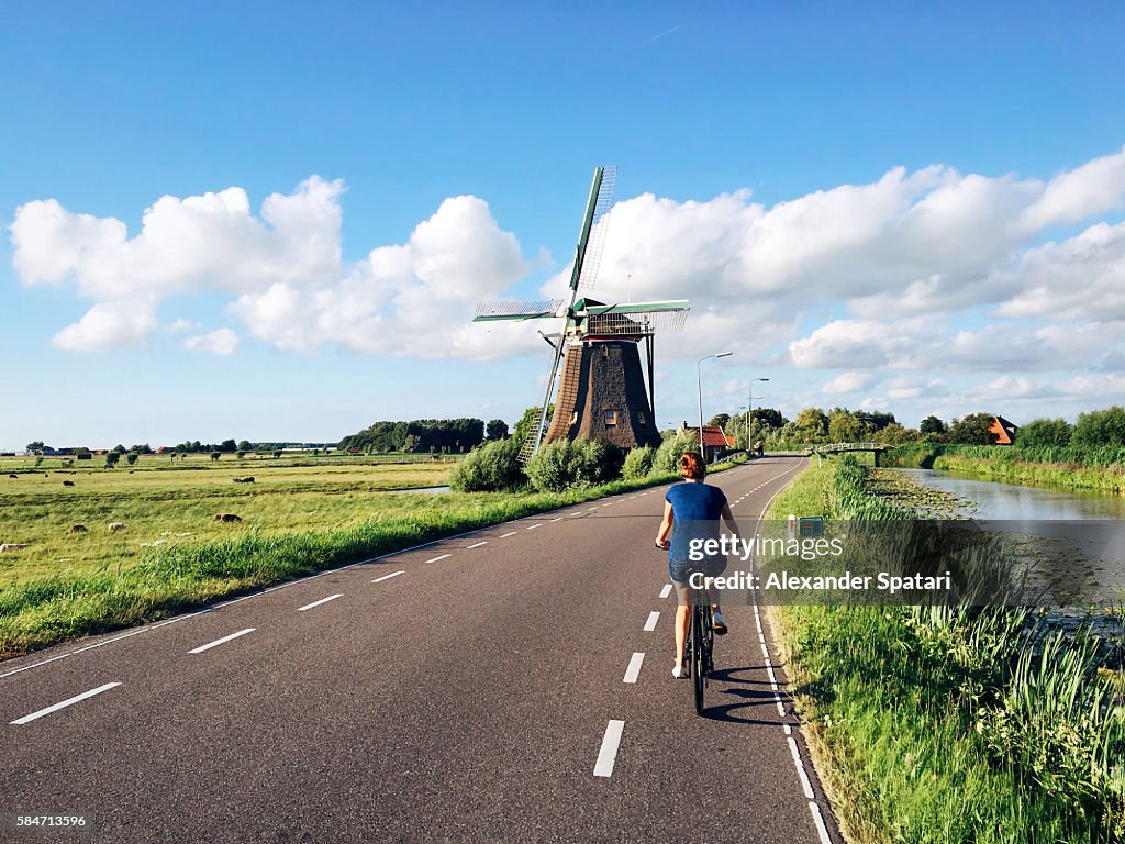 Young woman in shorts riding a bike near traditional Dutch windmill near Maasland, Holland, Netherlands
