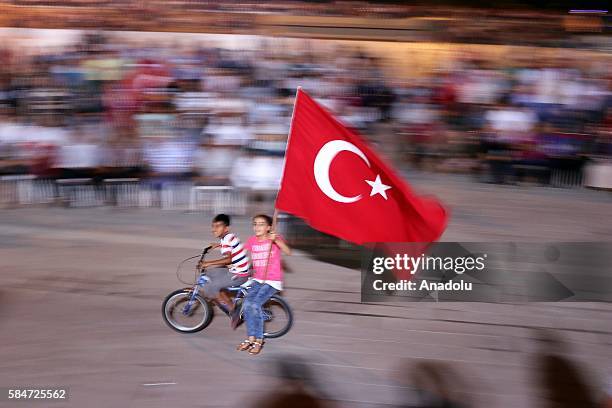 Two Children wave Turkish flag as they ride on bicycle as people gather to protest against July 15 failed military coup attempt, at Iskenderun...