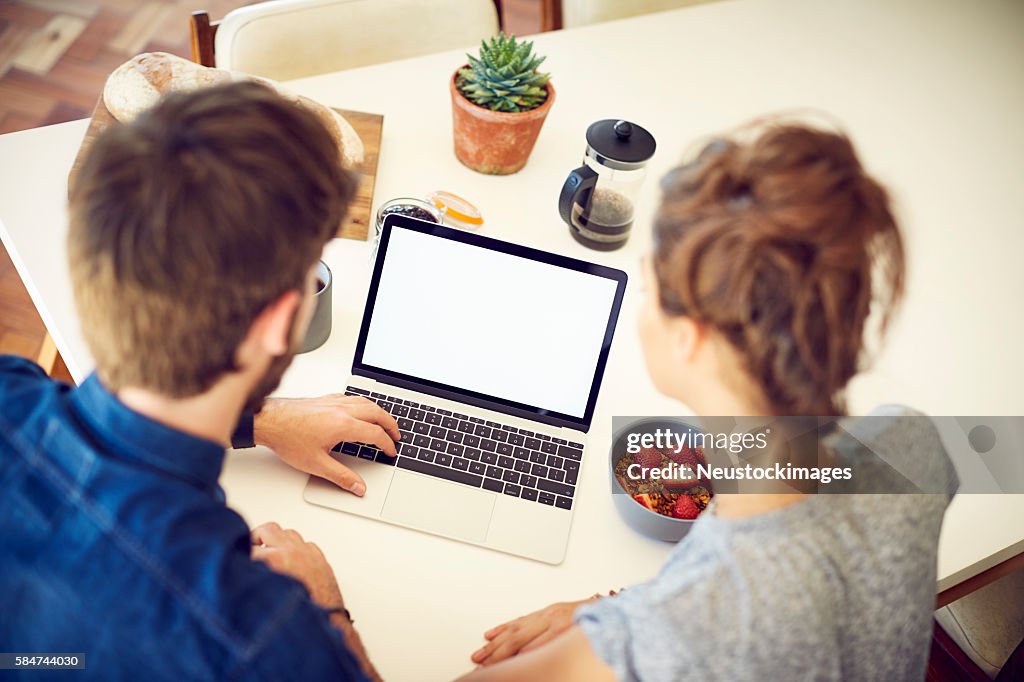 Über die Schulter des Paares mit Laptop zu Hause