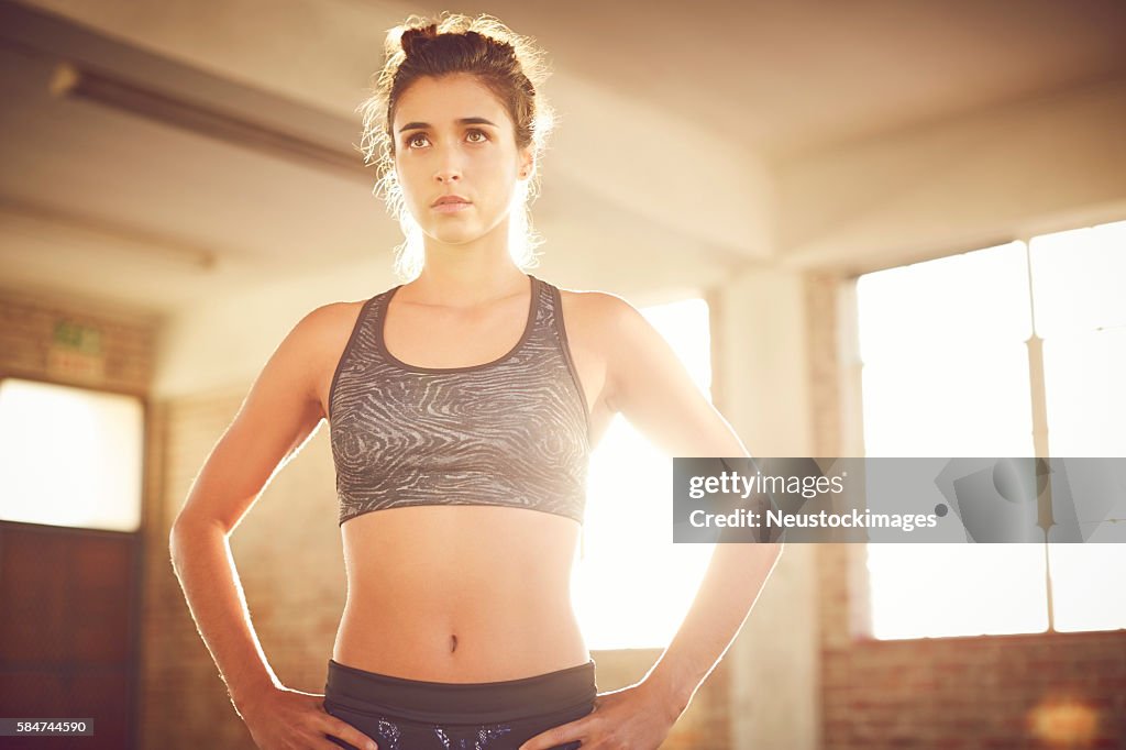 Determined fit young woman with hands on hips in gym