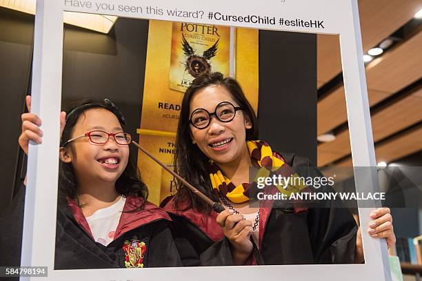 Mother and her daughter pose dressed up as Harry Potter characters in front of a poster advertising the new book 'Harry Potter and the Cursed Child'...