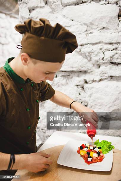 man pouring olive oil on to fresh greek salad - greek salad stock pictures, royalty-free photos & images