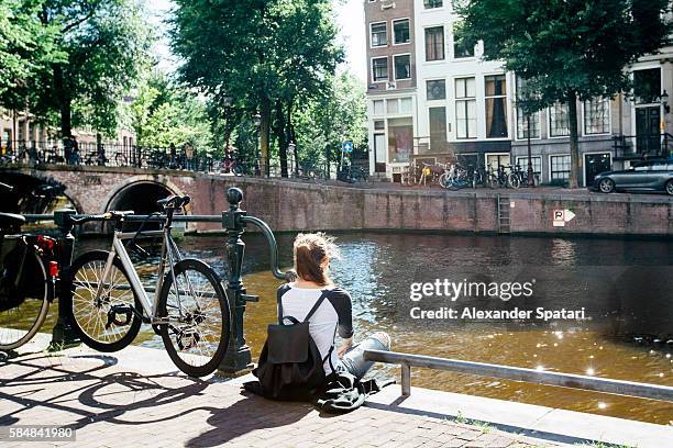 young girl sitting at the canal in amsterdam at sunset, netherlands - netherlands sunset stock pictures, royalty-free photos & images