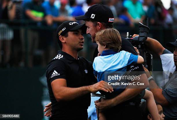 Jimmy Walker of the United States is congratulated on his victory by Jason Day of Australia while holding his son Beckett on the 18th green during...
