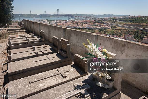 Graves and fading flowers overlook the Ponte 25 de Abril bridge and the district of Alacantara in the western Portuguese capital, on 14th July 2016,...
