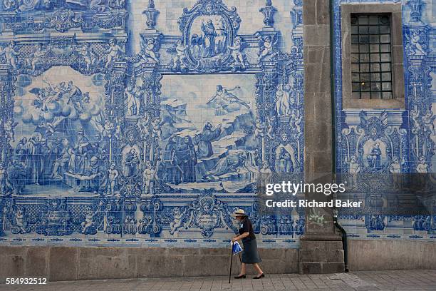 Elderly lady walks with sticks along the Rua de Fernandes Tomas with Azulejo tiles on the exterior of Capela Das Almas, on 20th July, in Porto,...