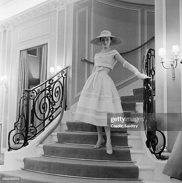 Model wearing a white organdie dress by Dior, Paris, March 1956. The dress is bound with white grosgrain ribbons, showing the high Empire bosom and...