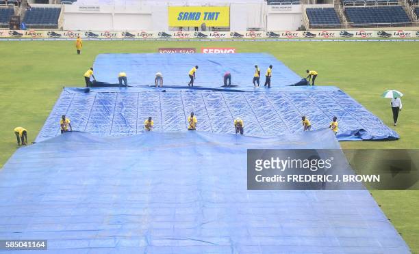 Groundskeeprs cover the pitch as rain delays the 2nd Test cricket match on day three between India and the West Indies on August 1, 2016 at Sabina...