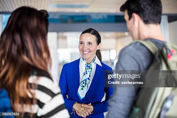 hostess aerea che aiuta giovane coppia in aeroporto - flight attendant serving foto e immagini stock