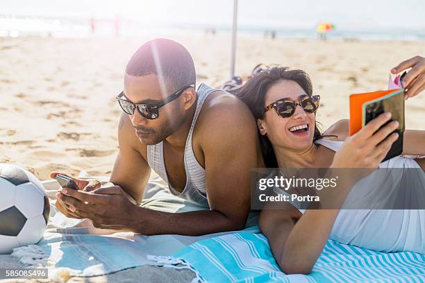 couple wearing sunglasses relaxing at beach - couple on beach sunglasses stockfoto's en -beelden