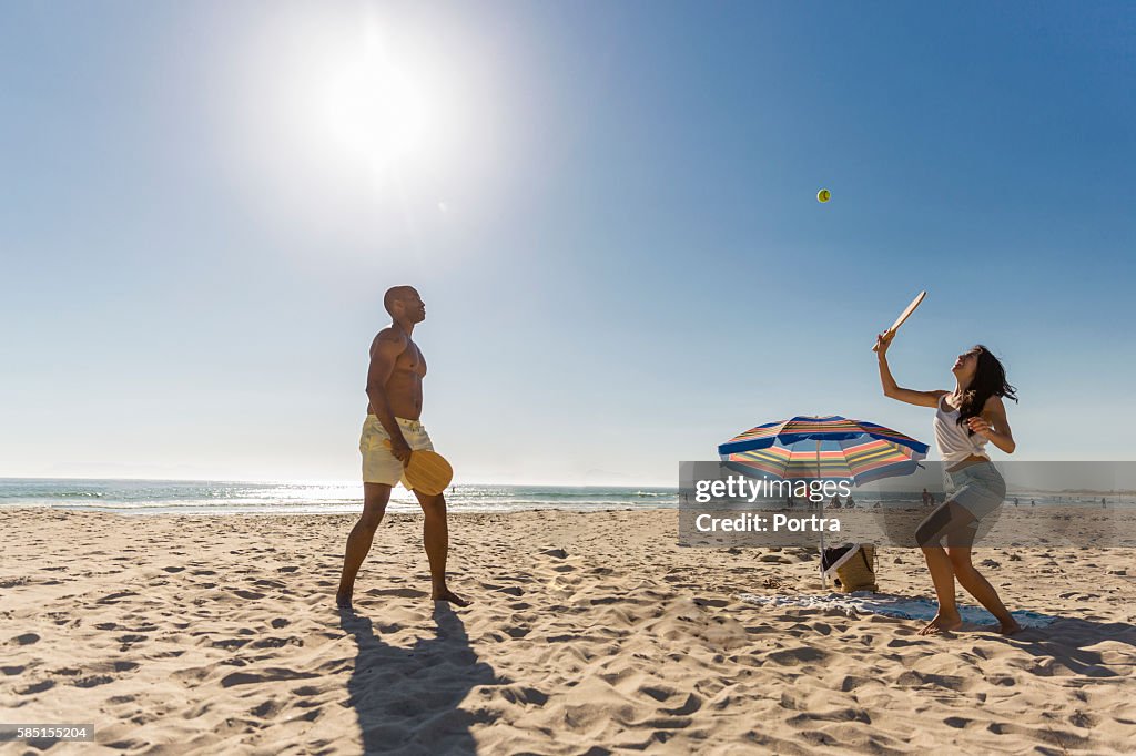 Coppia che gioca a tennis in spiaggia contro cielo sereno