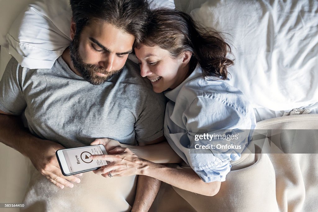 Couple au lit à l’aide de l’application cafetière sur téléphone intelligent