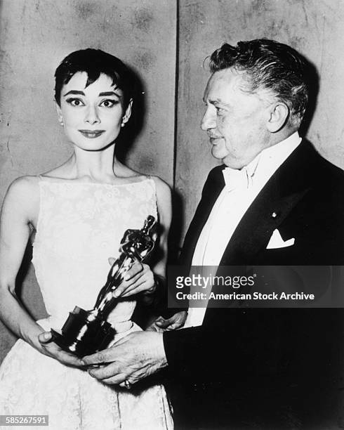 Actress Audrey Hepburn holding her Best Actress Oscar for the film 'Roman Holiday', with presented Jean Hersholt, at the 26th Academy Awards, New...