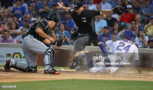 Home plate umpire Mike Muchlinski signals that Dexter Fowler of the Chicago Cubs is safe at home plate after J.T. Realmuto of the Miami Marlins...
