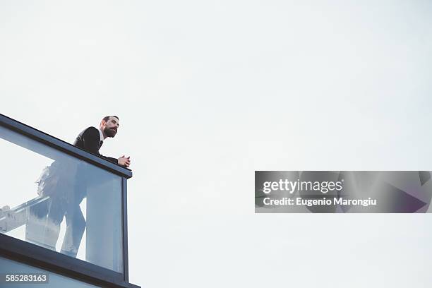 low angle view of businessman looking out from office balcony - ein mann allein stock-fotos und bilder