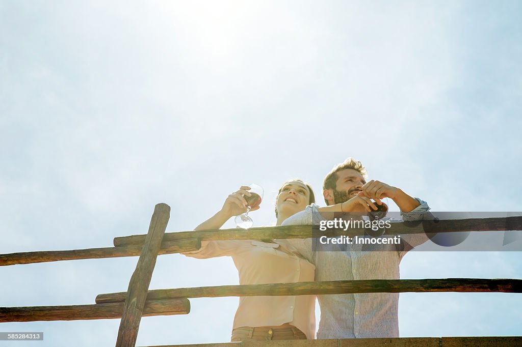 Low angle view of young couple holding wine glasses looking away