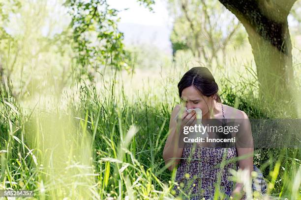 young woman in tall grass sneezing into handkerchief - allergy season stock pictures, royalty-free photos & images