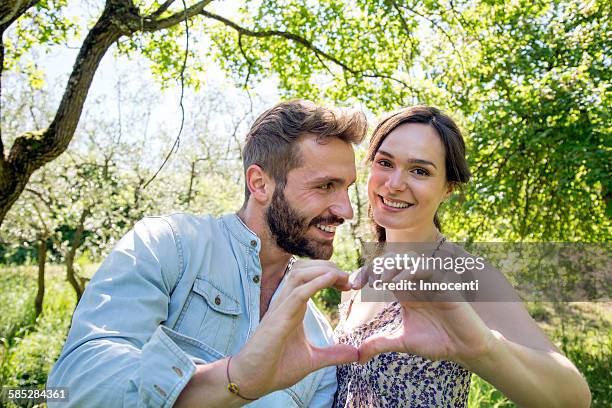 young couple making heart shape with hands, looking at camera smiling - love symbol #2 stock pictures, royalty-free photos & images