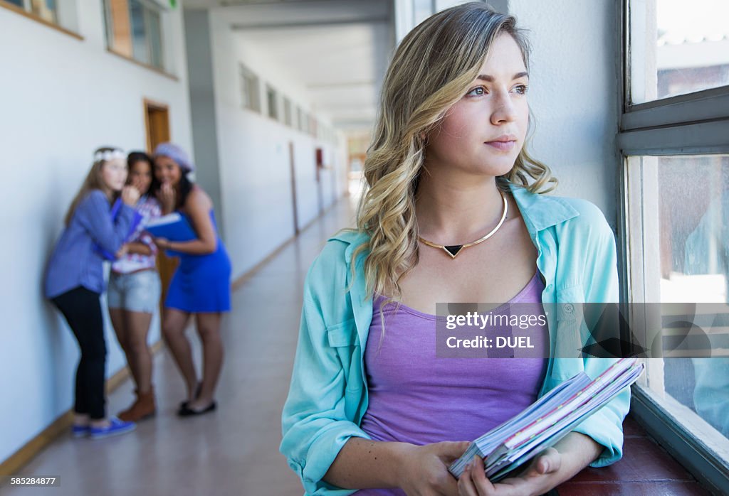 Student looking out window, friends gossiping in background